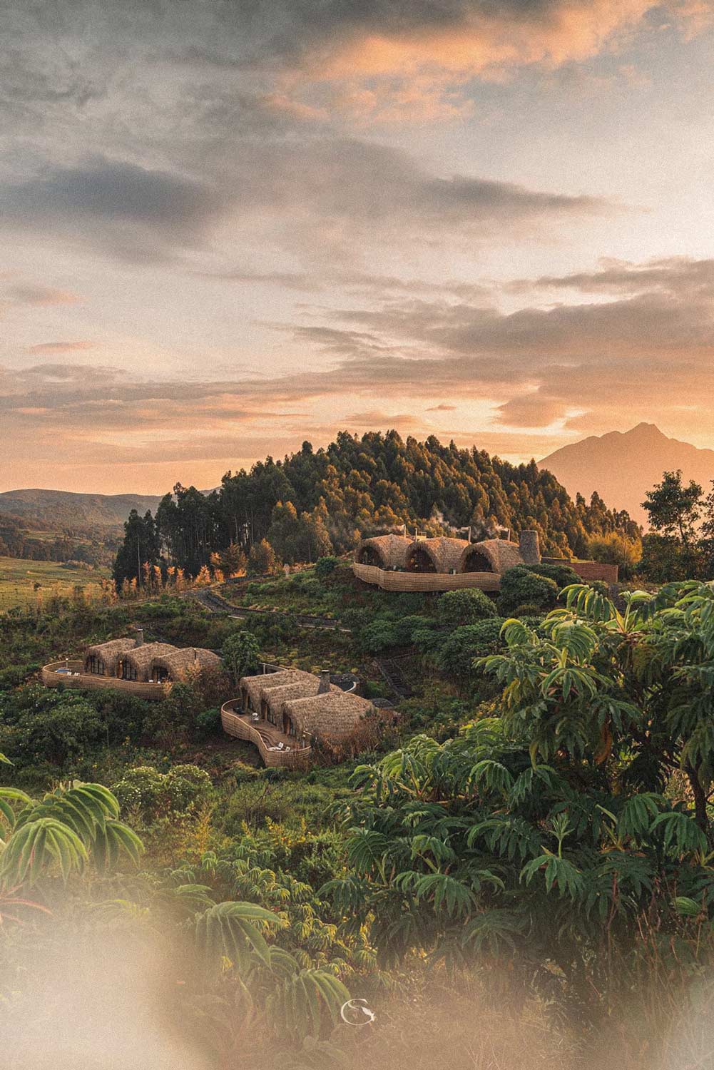 Domed lodge villas on a forested hillside beneath a volcano at sunset
