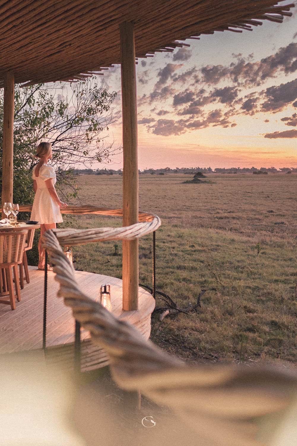 A guest on a thatched deck looking out over the open plains at dusk